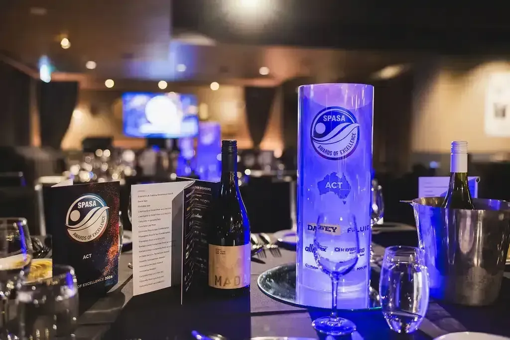 Table setting at a formal event, with wine bottles, menus, glasses, and a lit centerpiece.