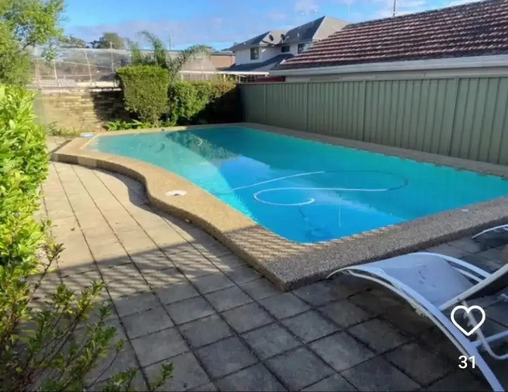 Swimming pool with blue water and stone patio surrounded by fence and foliage.