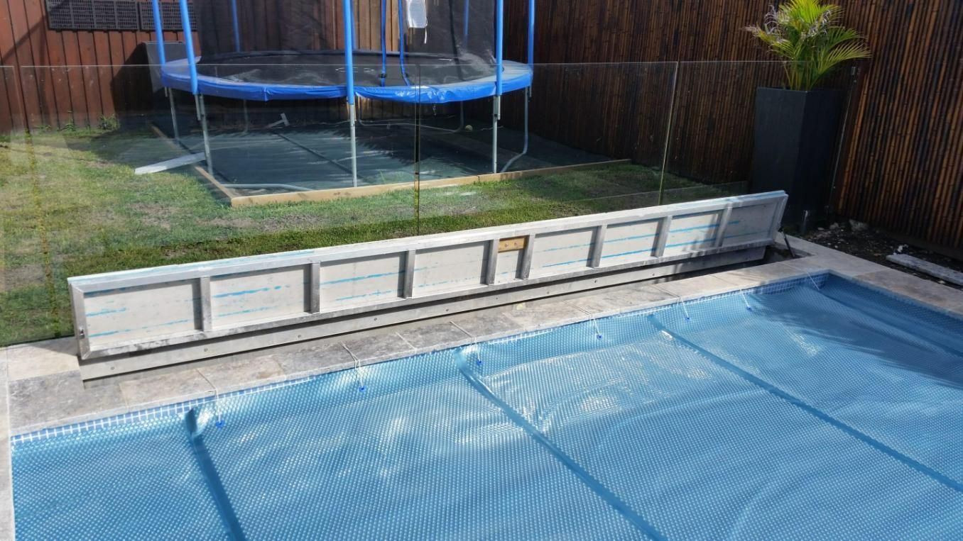 A pool with blue cover, a trampoline, and a lawn.