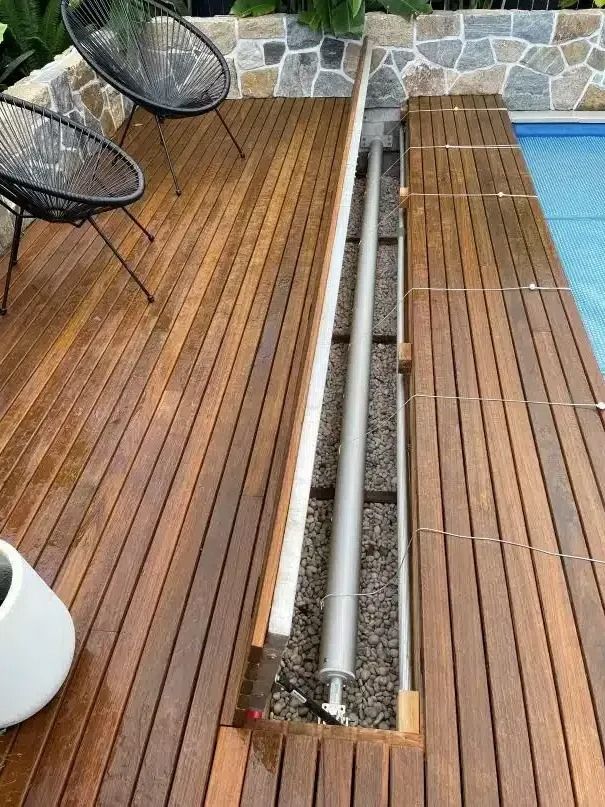 Wooden pool deck with a retractable pool cover mechanism; two chairs nearby.