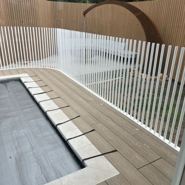 White picket fence surrounding a pool deck, with wooden background.