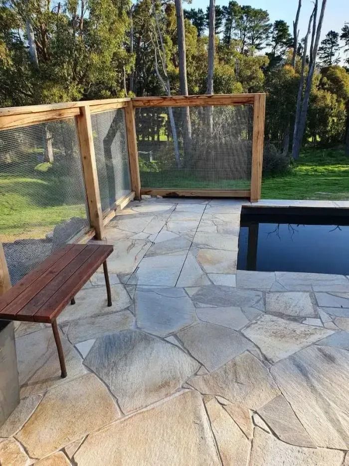 Stone patio with a wooden bench and wire mesh fence surrounding a dark pool.