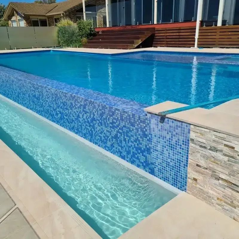 Swimming pool with blue tiles, built-in overflow channel, and a house in the background.