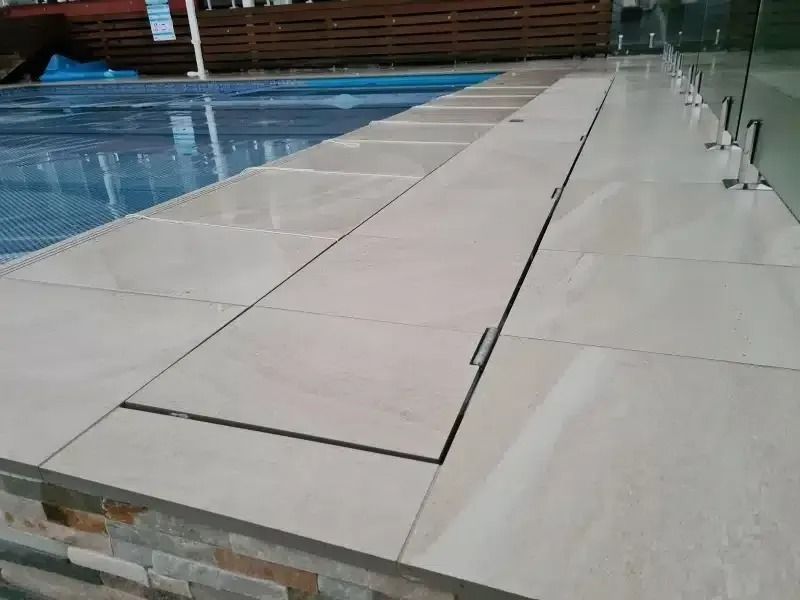 Poolside area with light beige tiles, a rectangular pool, and a partially open compartment.