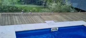 A blue swimming pool with a wooden deck and greenery in the background.
