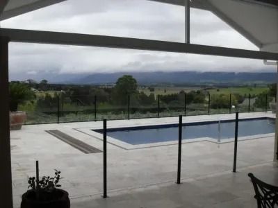 Pool with black fence, overlooking a valley under a cloudy sky.