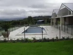 Pool and house on a grassy property under a cloudy sky. Black fencing surrounds the pool and house.