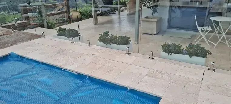 A pool with a blue cover, next to a patio with planters and glass fencing.