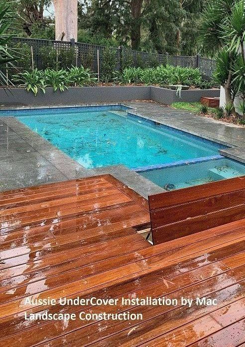 Wooden deck and pool with blue water on a rainy day. Landscaping in background.