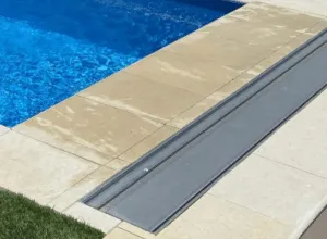 Poolside view of a blue pool and tan concrete deck with a gray pool cover mechanism.
