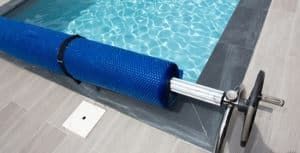 Blue pool cover rolled up on a pool's edge, with a hand crank.