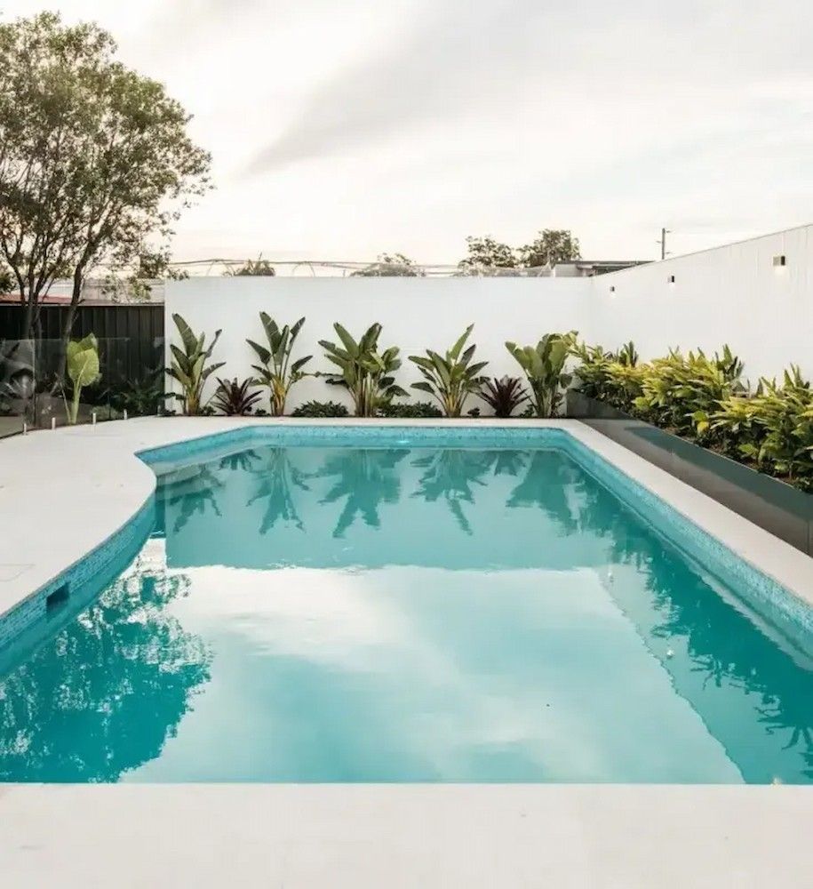 Pool with clear water, surrounded by white walls and lush greenery. Overcast sky.