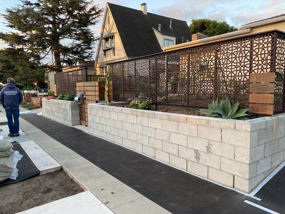 A man is walking down a sidewalk next to a brick wall.