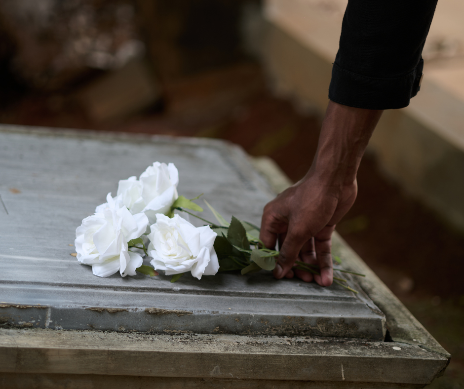 A hand places a small bouquet of three white roses onto a stone grave marker.