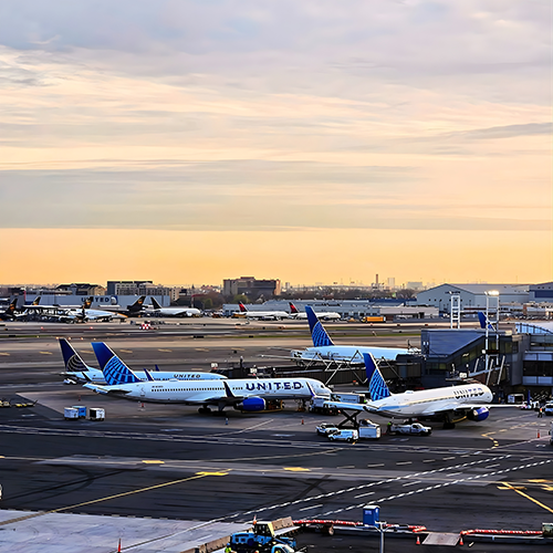 Several United Airlines planes parked at an airport terminal during a soft sunset.