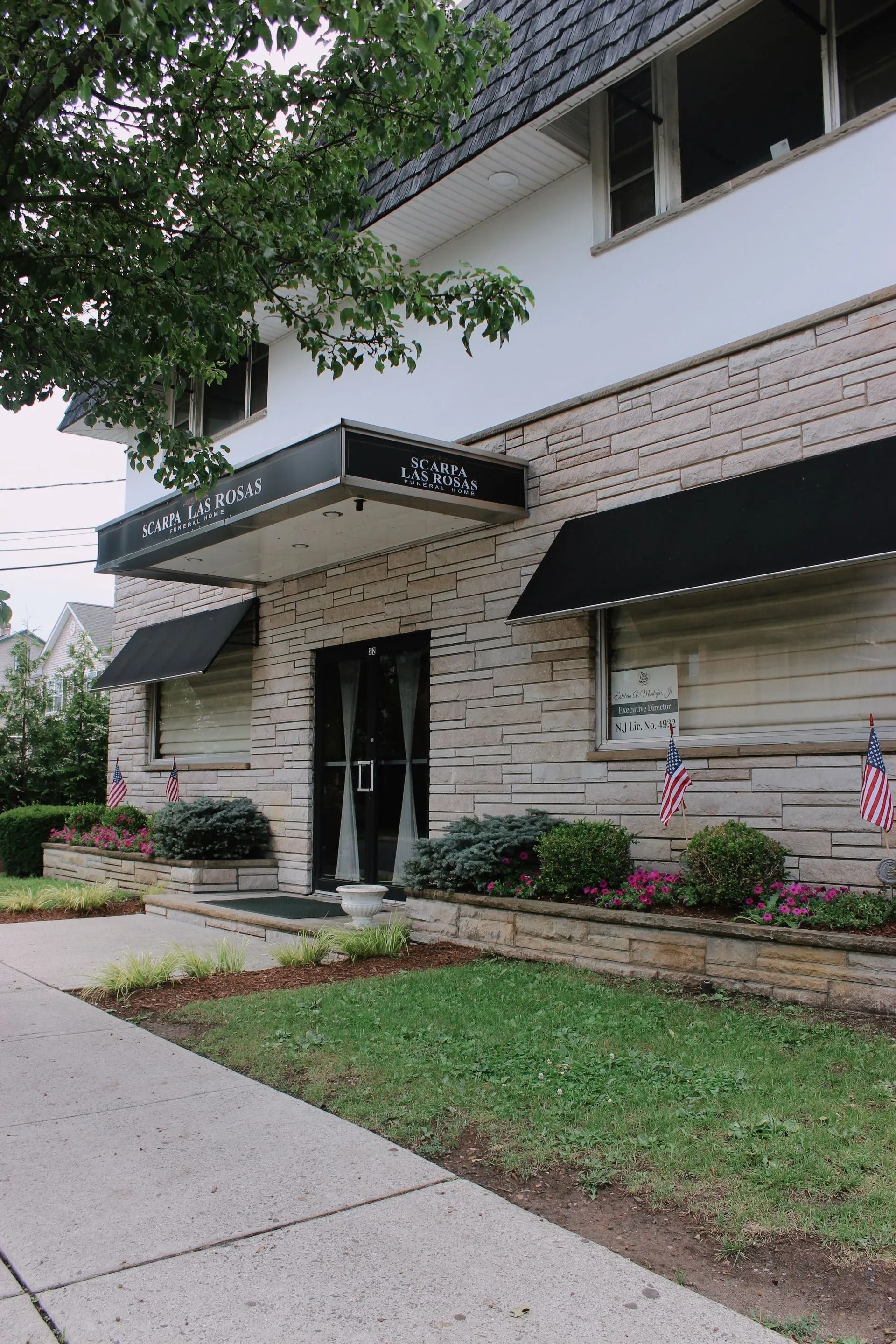 A brick building with black awnings, a central entryway under a flat canopy, and American flags displayed on the front wall.