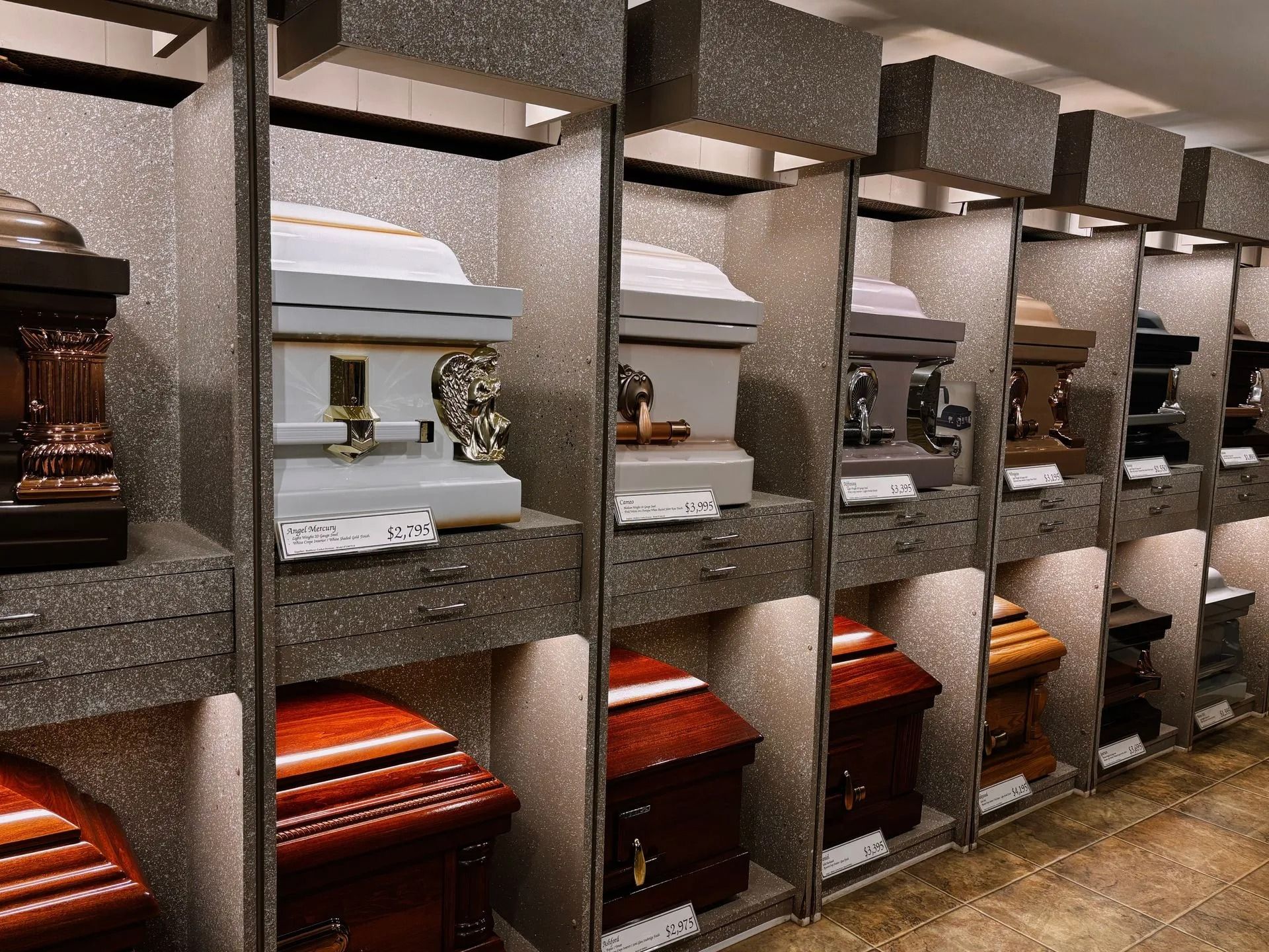 A display room showing rows of various wooden and metal caskets arranged on shelves.