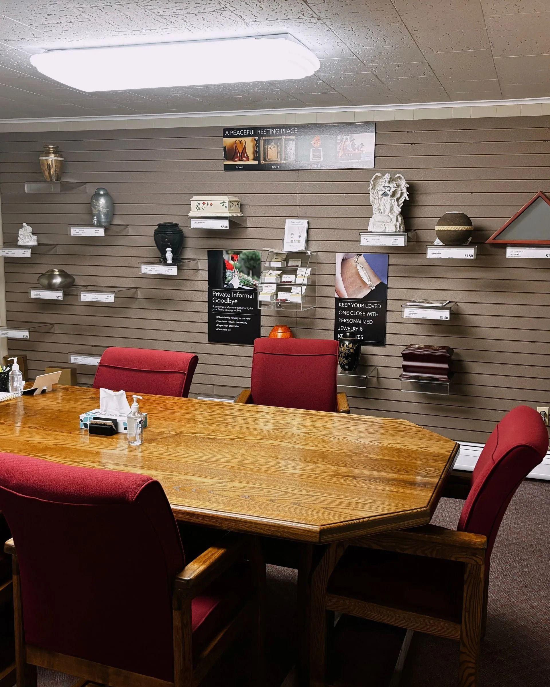 A conference room with a large wooden table, red chairs, and wall-mounted shelves displaying various decorative items.