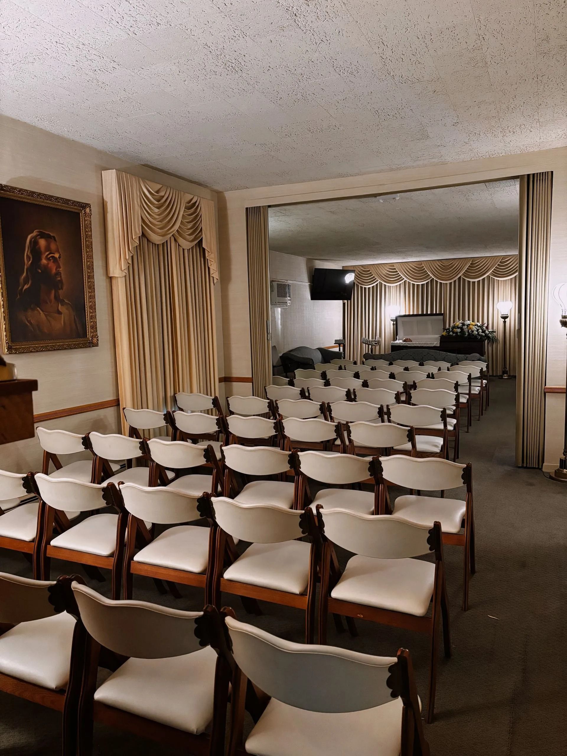 Rows of chairs in a room with a mirror reflecting a second section, beige curtains, and a framed portrait on the wall.