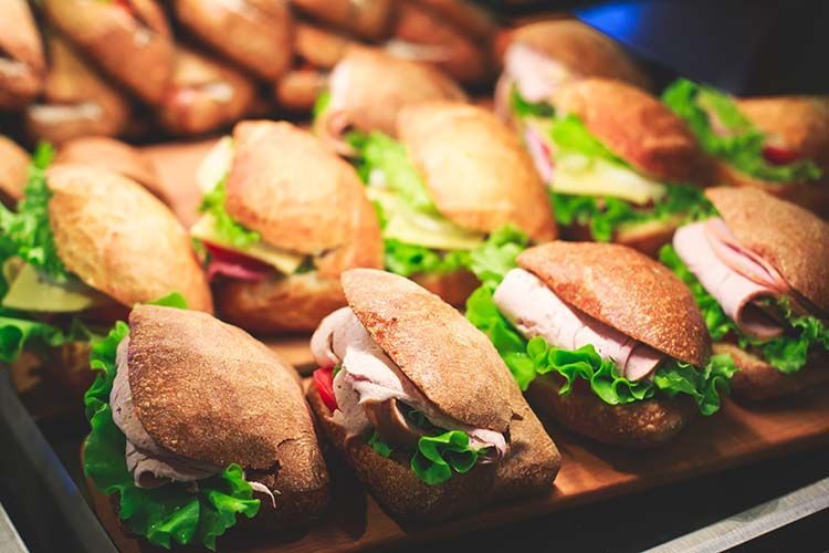 A display tray of freshly prepared sandwiches on crusty brown rolls filled with ham, cheese, and lettuce.