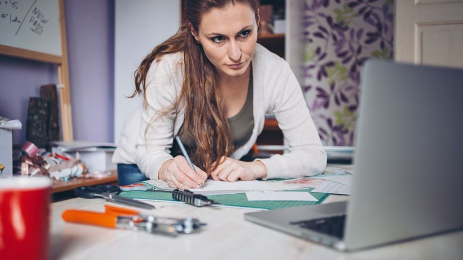 Self-employed designer working from home, making notes about her self-employment tax.