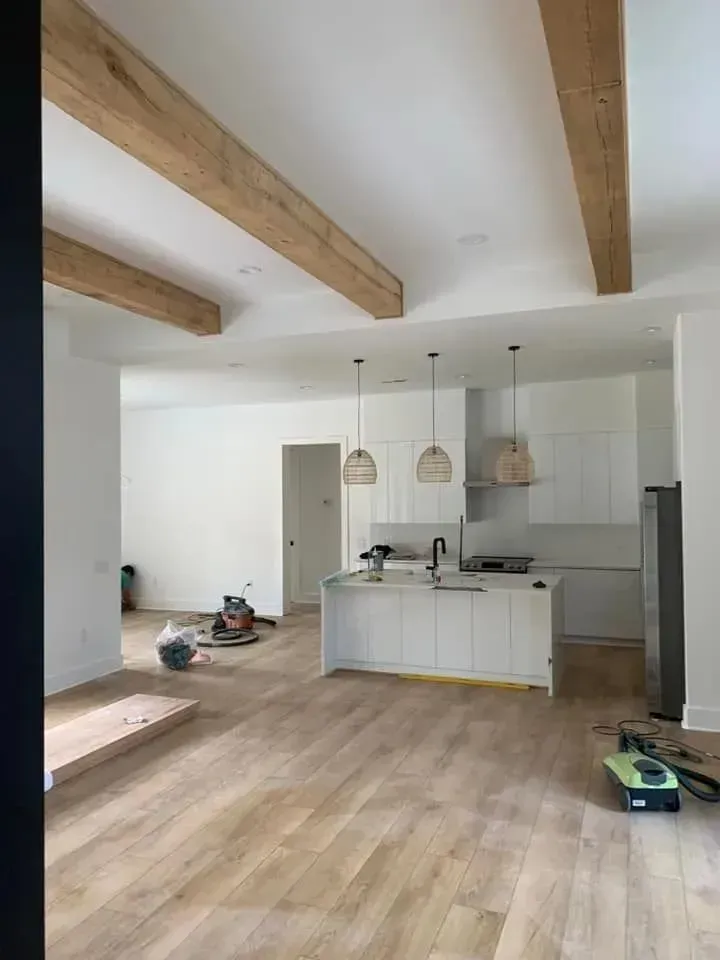 A kitchen with white cabinets and wooden beams is being remodeled.