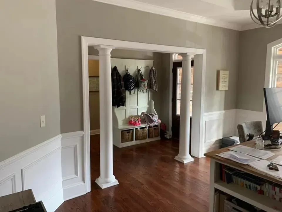 A living room with hardwood floors , columns , a desk and a computer.