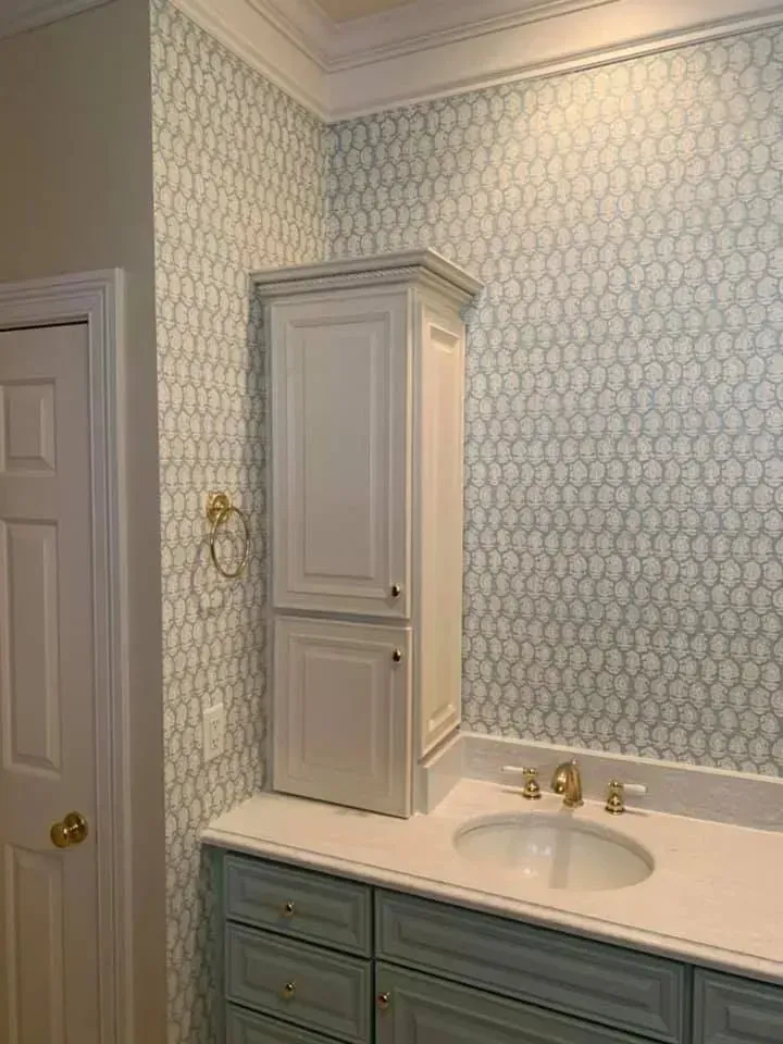 A bathroom with a sink , cabinets , and wallpaper.