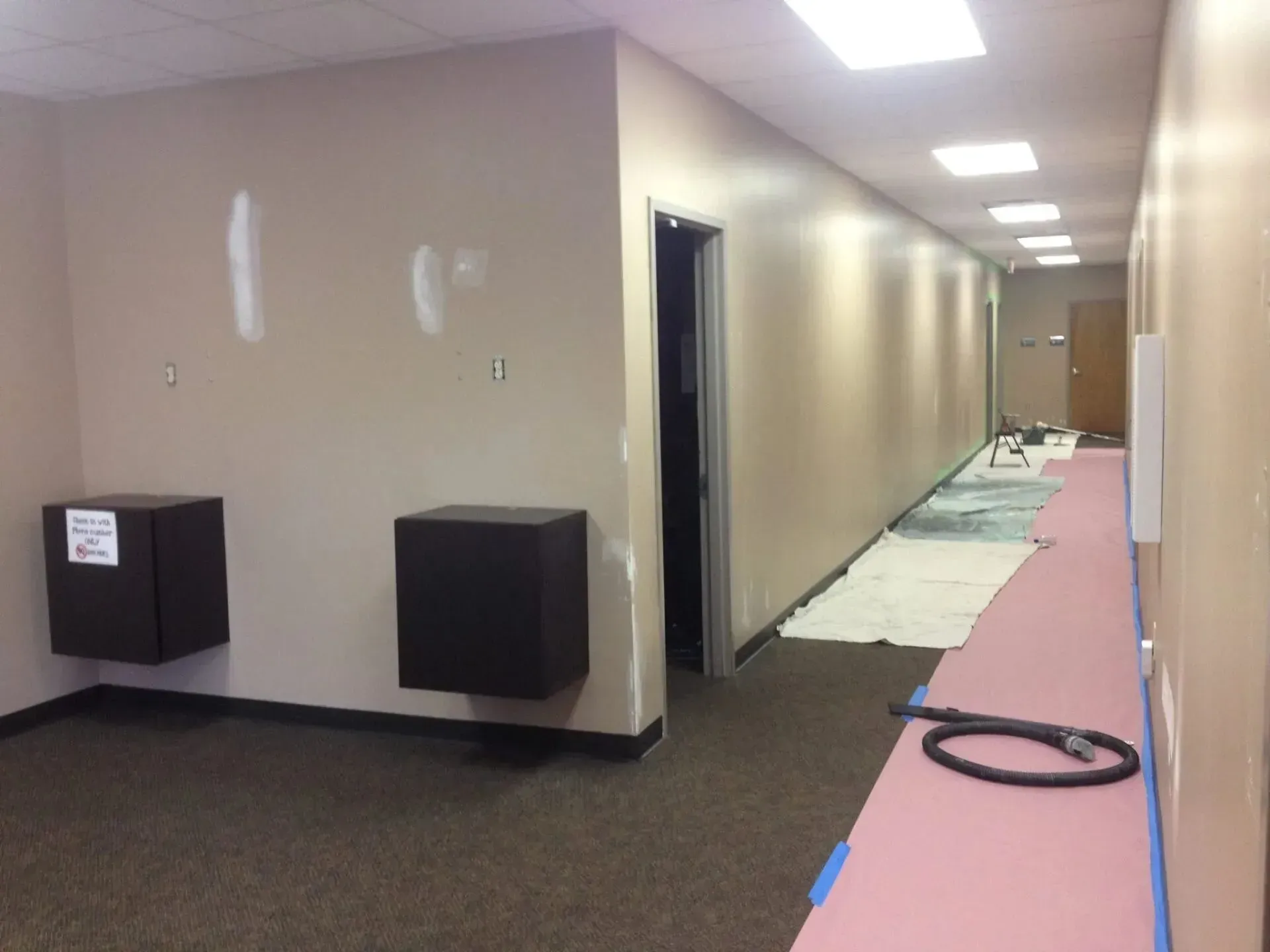 A long hallway with pink carpet and a vacuum cleaner on the floor.