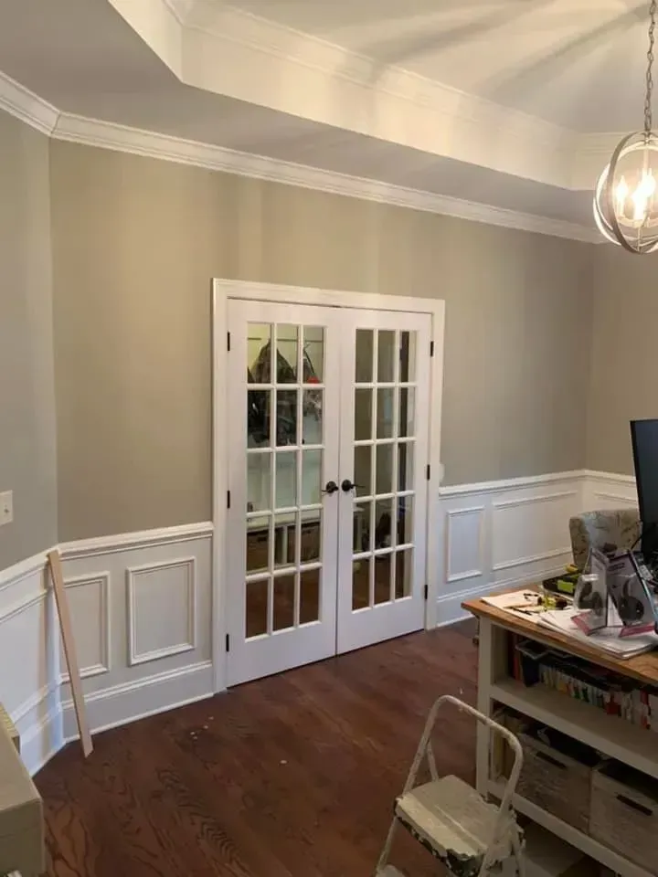A room with a desk , chair , computer and french doors.