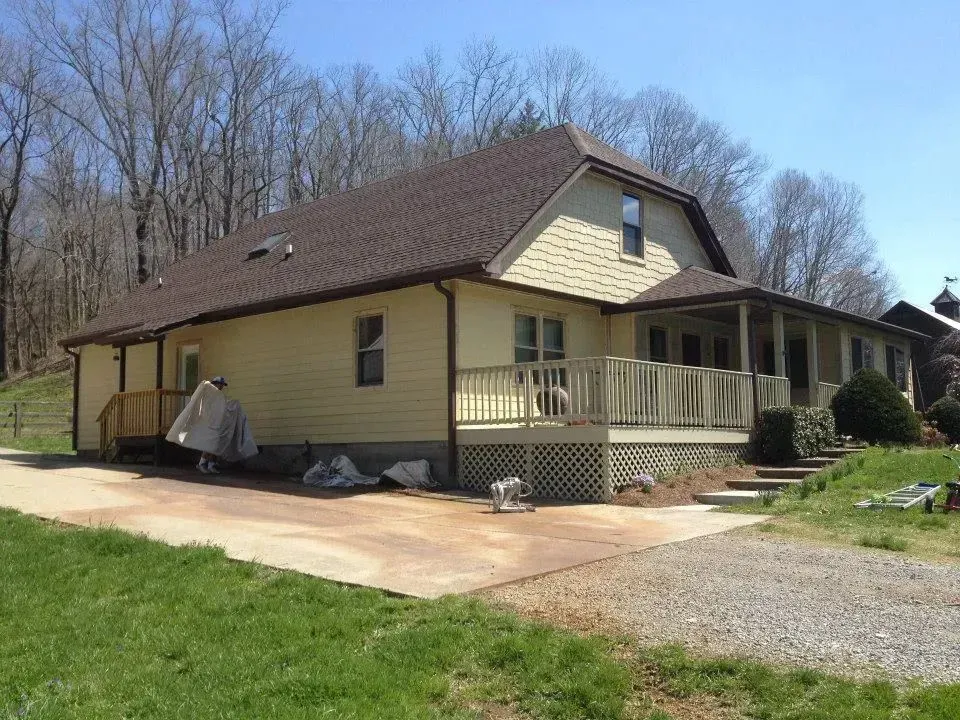 A yellow house with a brown roof and a porch