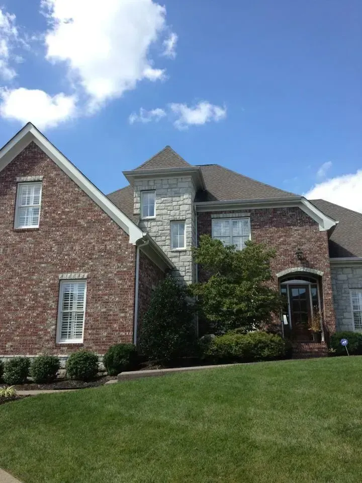 A large brick and stone house with a lush green lawn in front of it