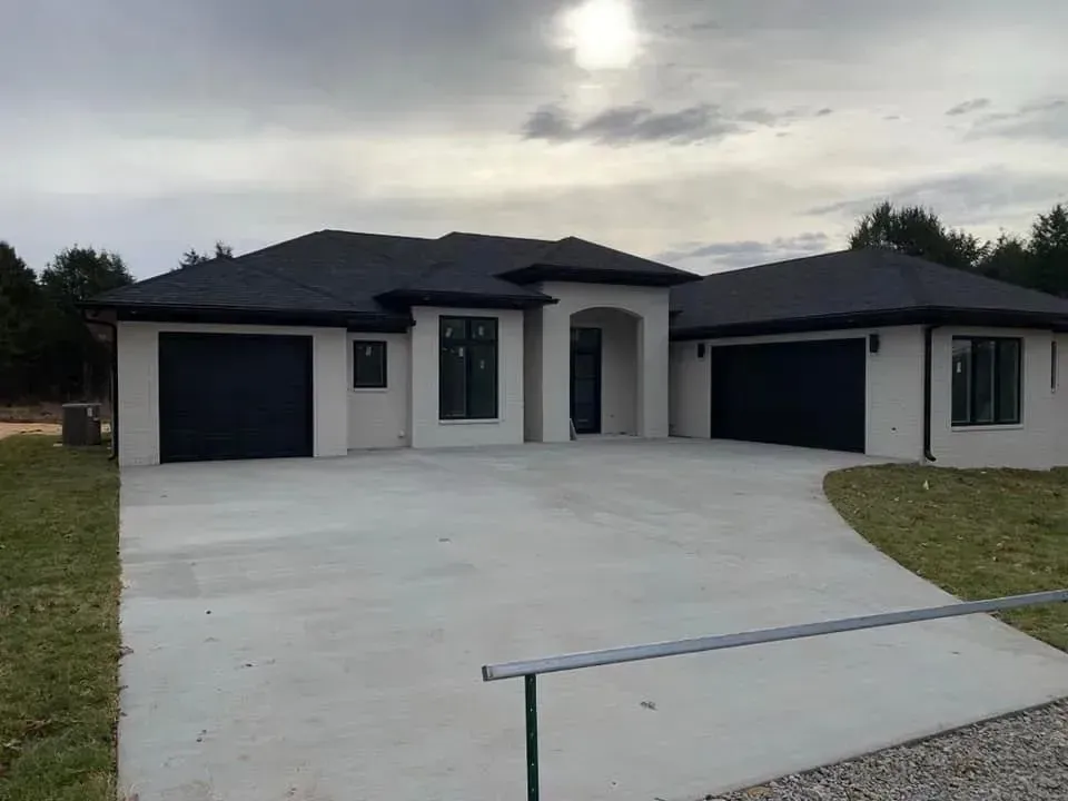 A large white house with a black garage door and a concrete driveway.