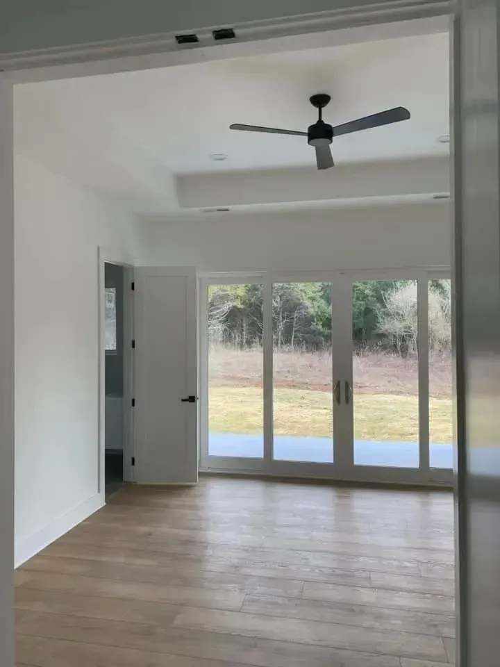 An empty room with a ceiling fan and sliding glass doors.