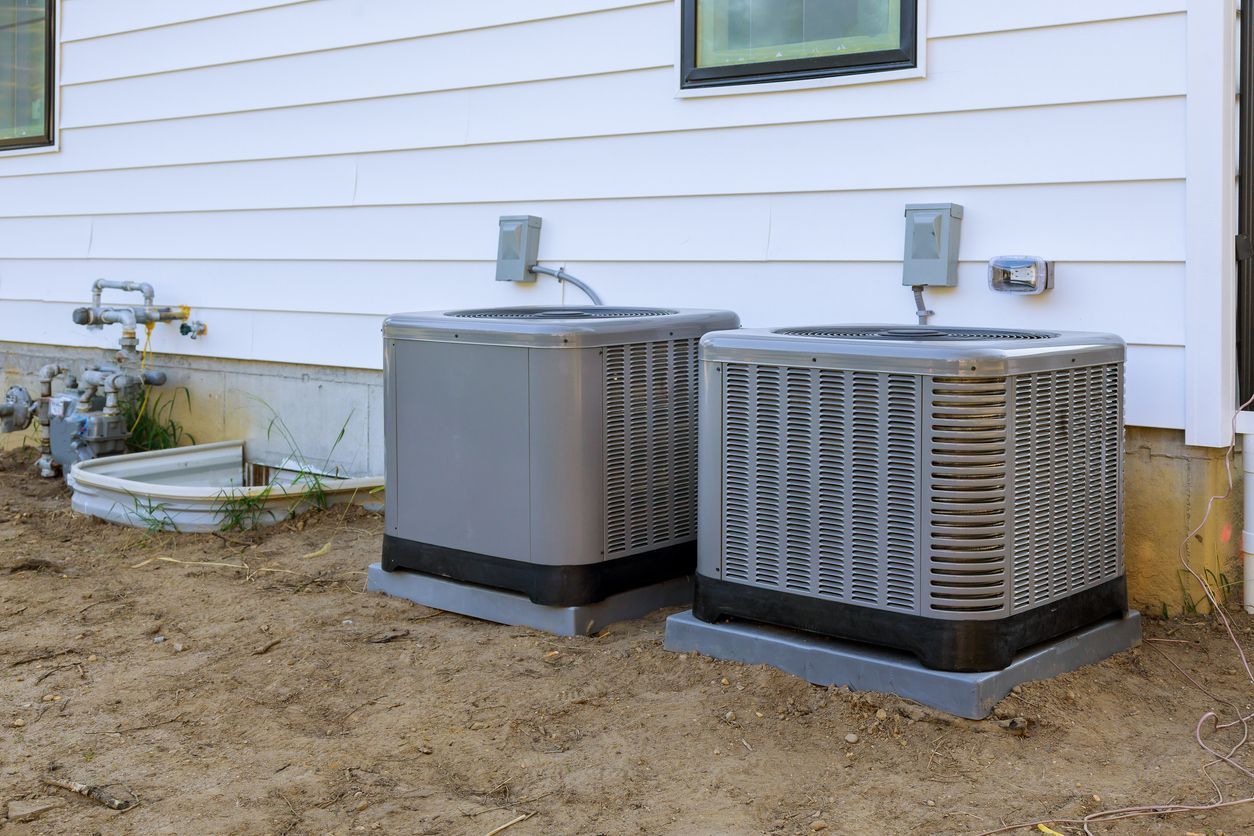 Two air conditioners are sitting on the side of a house.