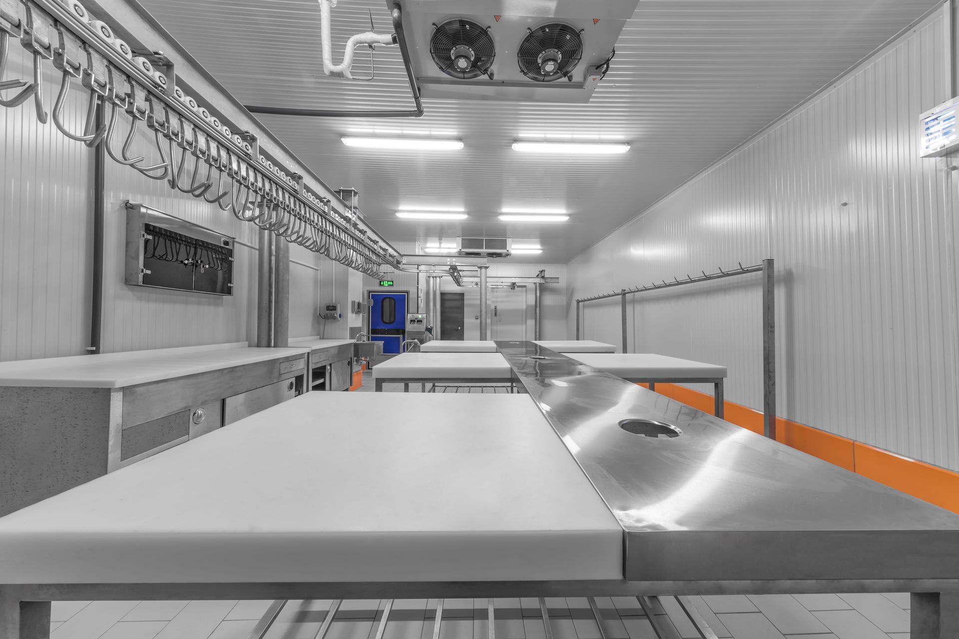 An empty, sterile butcher shop with stainless steel tables, hanging hooks, and refrigeration units.