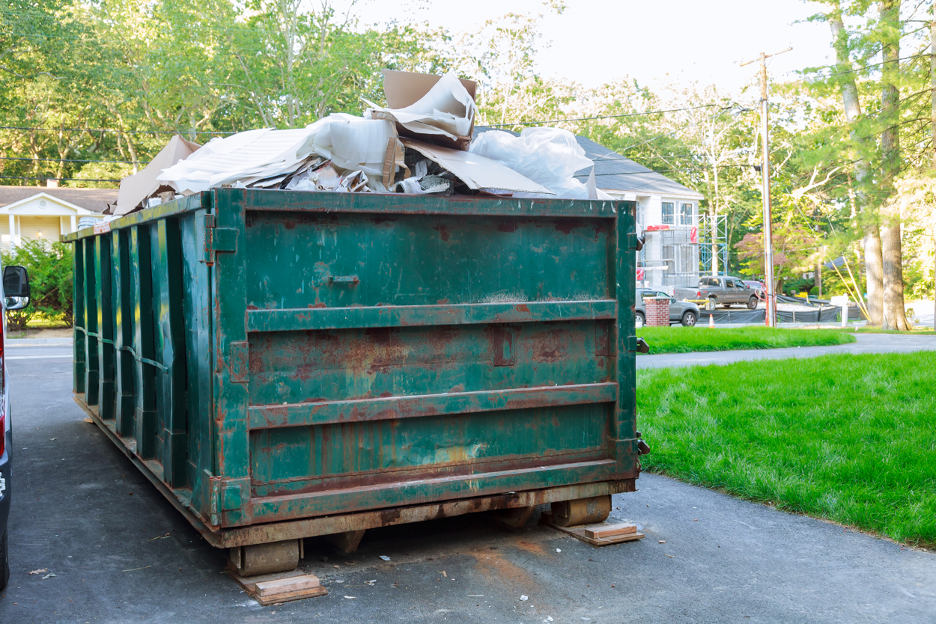 Green dumpster filled with debris on a residential driveway.