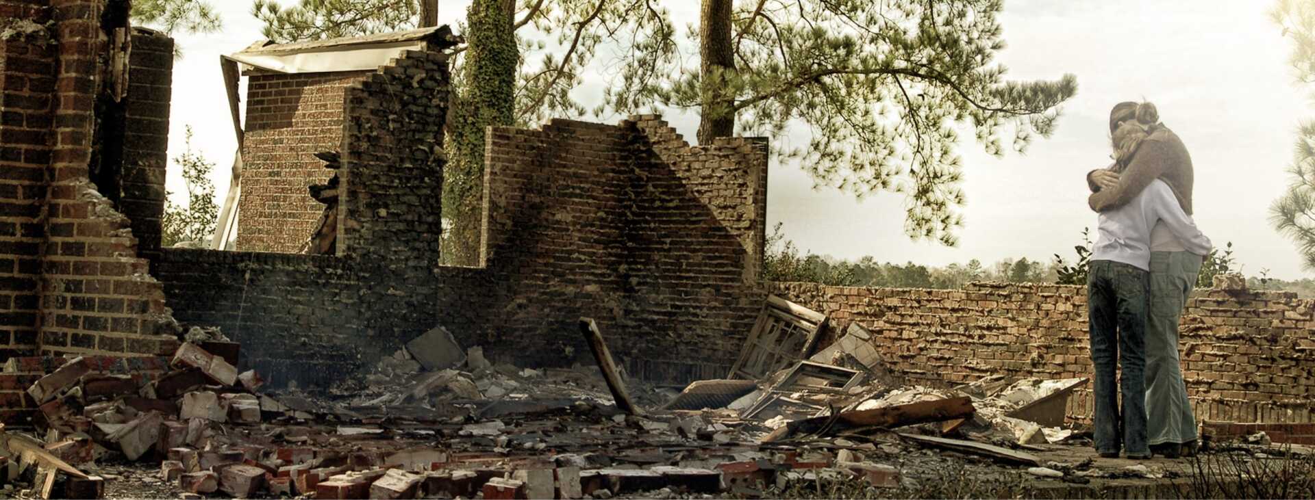 Deux personnes s'enlacent devant les ruines calcinées d'un bâtiment en briques après un incendie.