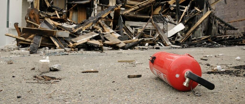 Un extincteur rouge gît sur les débris d'une structure incendiée.