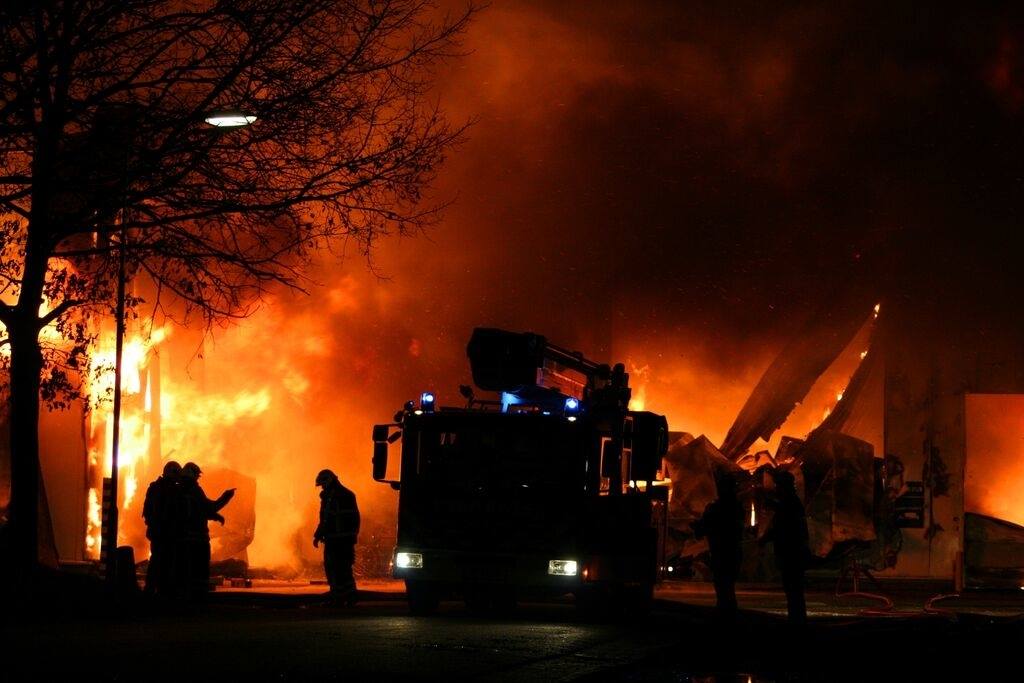 Des pompiers luttent contre un important incendie de bâtiment en pleine nuit ; les flammes et la fumée dominent la scène.