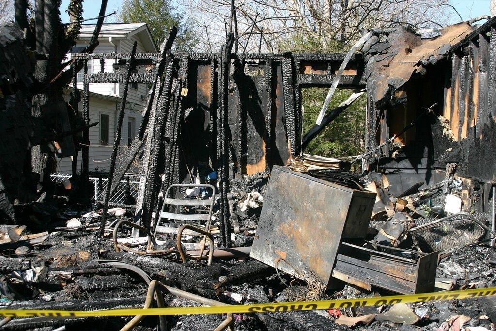 Vestiges calcinés d'une structure après un incendie, avec des poutres noircies et des débris.