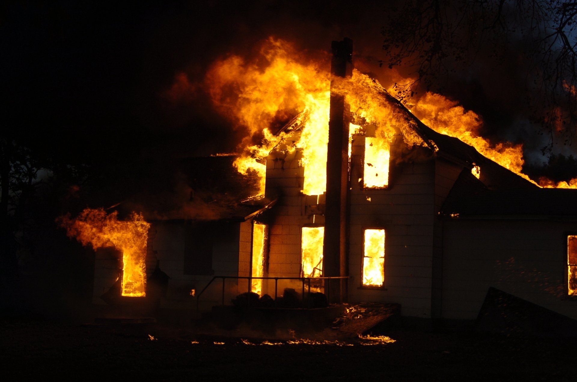 La maison est en flammes en pleine nuit. Des flammes orange vif jaillissent des fenêtres et du toit.