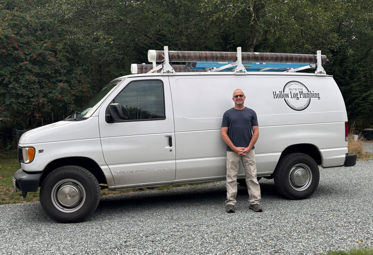 Man standing beside a white van with a roof rack. The van has business lettering on the side.
