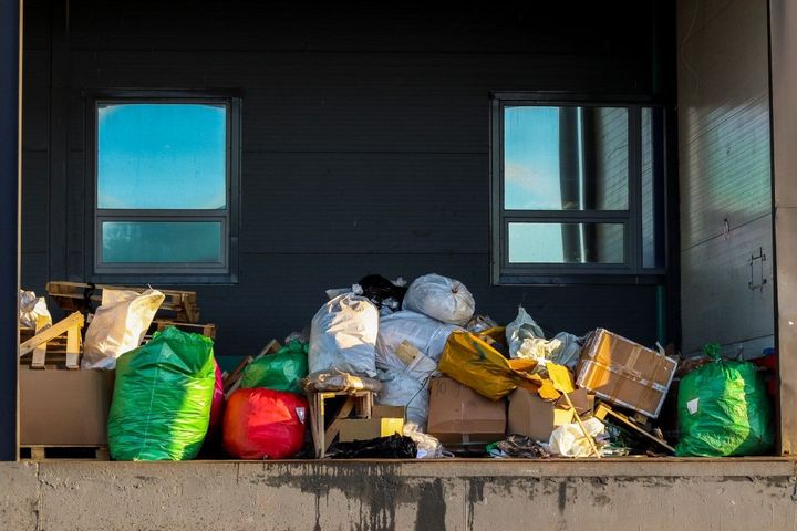 Overflowing trash bags and cardboard piled on a loading dock in front of a dark building