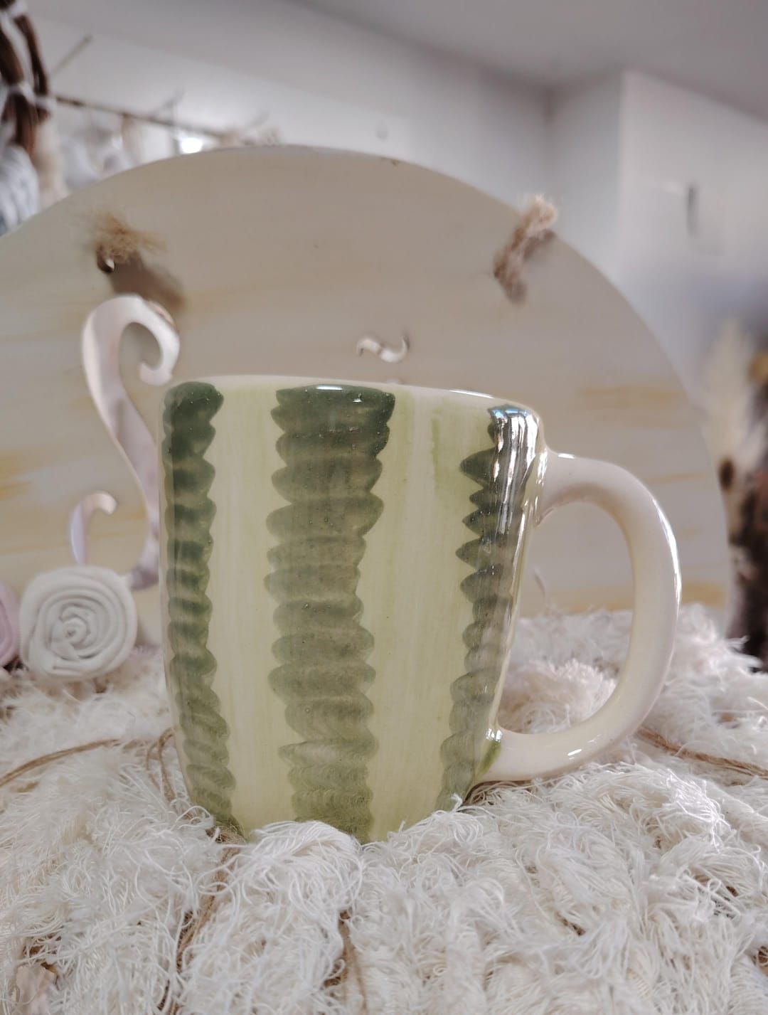 Taza de color crema con rayas verticales verdes, colocada sobre una superficie blanca esponjosa.