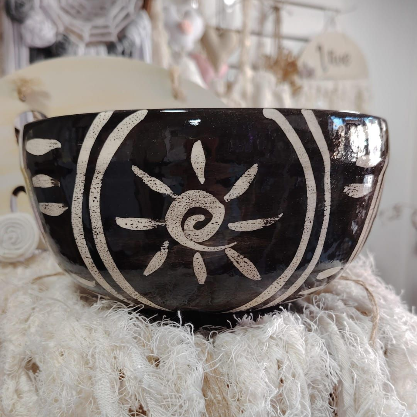 Cuenco de cerámica negra con diseño de sol blanco, colocado sobre una tela tejida.