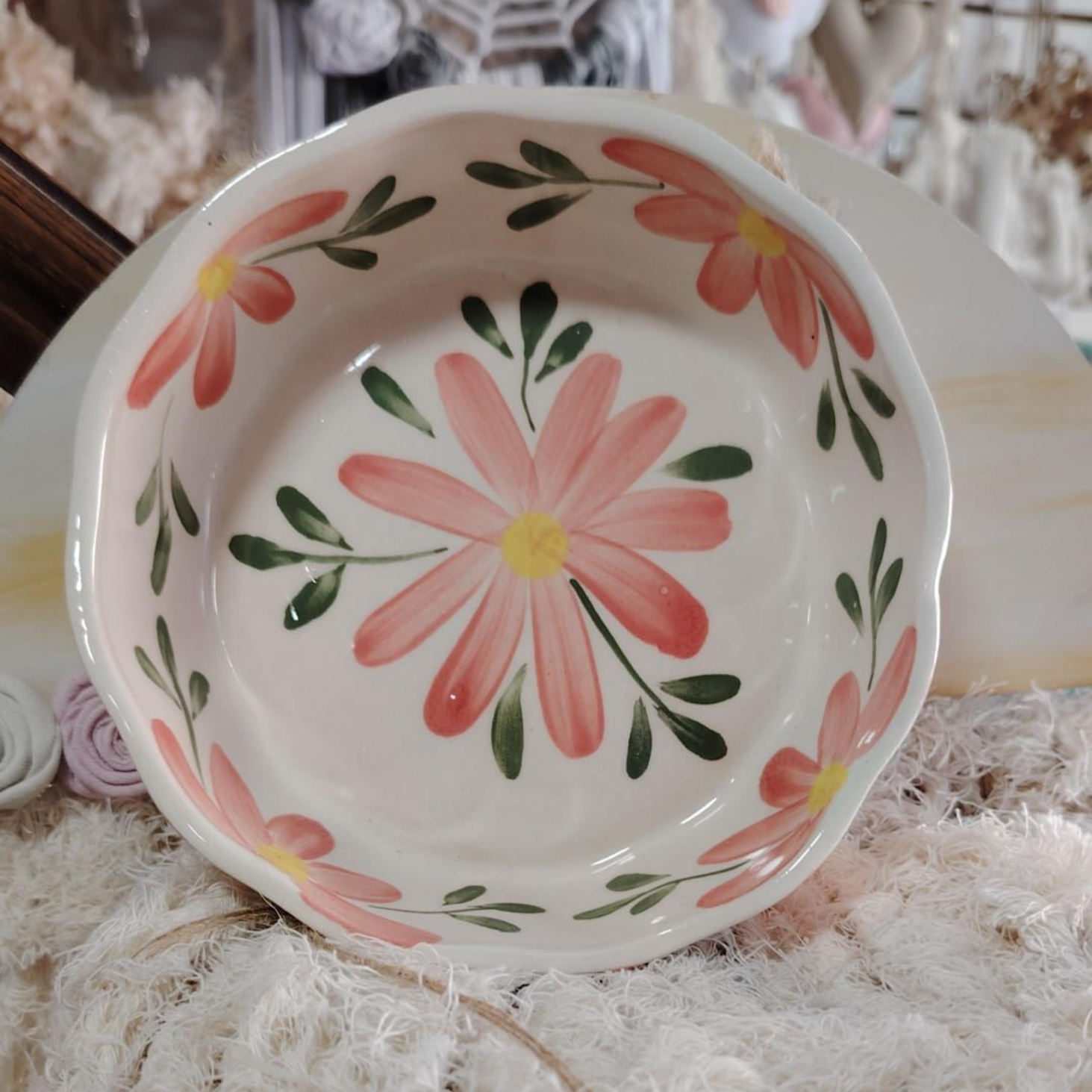 Cuenco de cerámica pintado a mano con margaritas rosas y hojas verdes sobre fondo blanco.