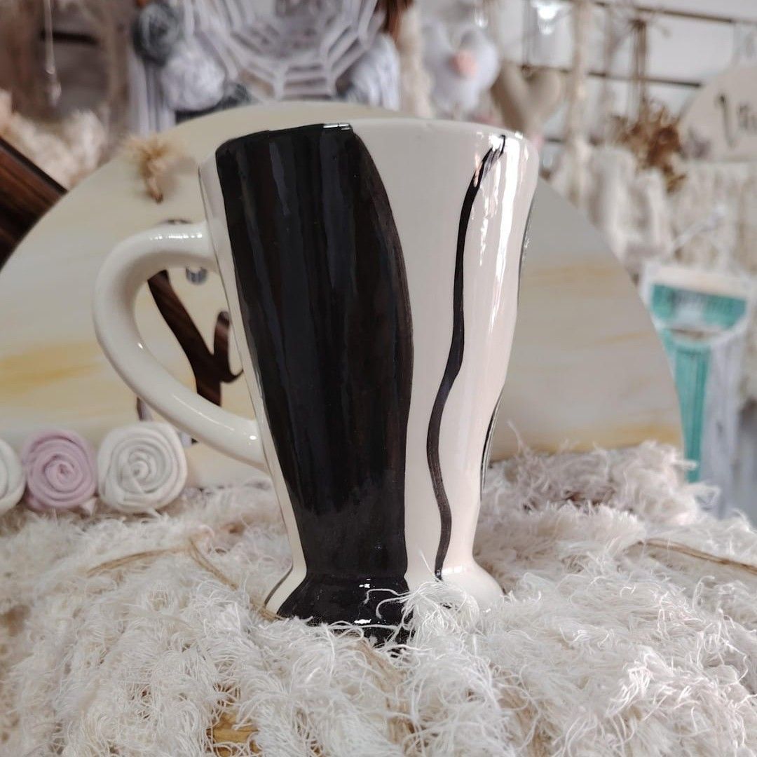 Taza de cerámica blanca con diseños estampados en rojo, rosa y gris, sobre una tela tejida a crochet de color blanco.