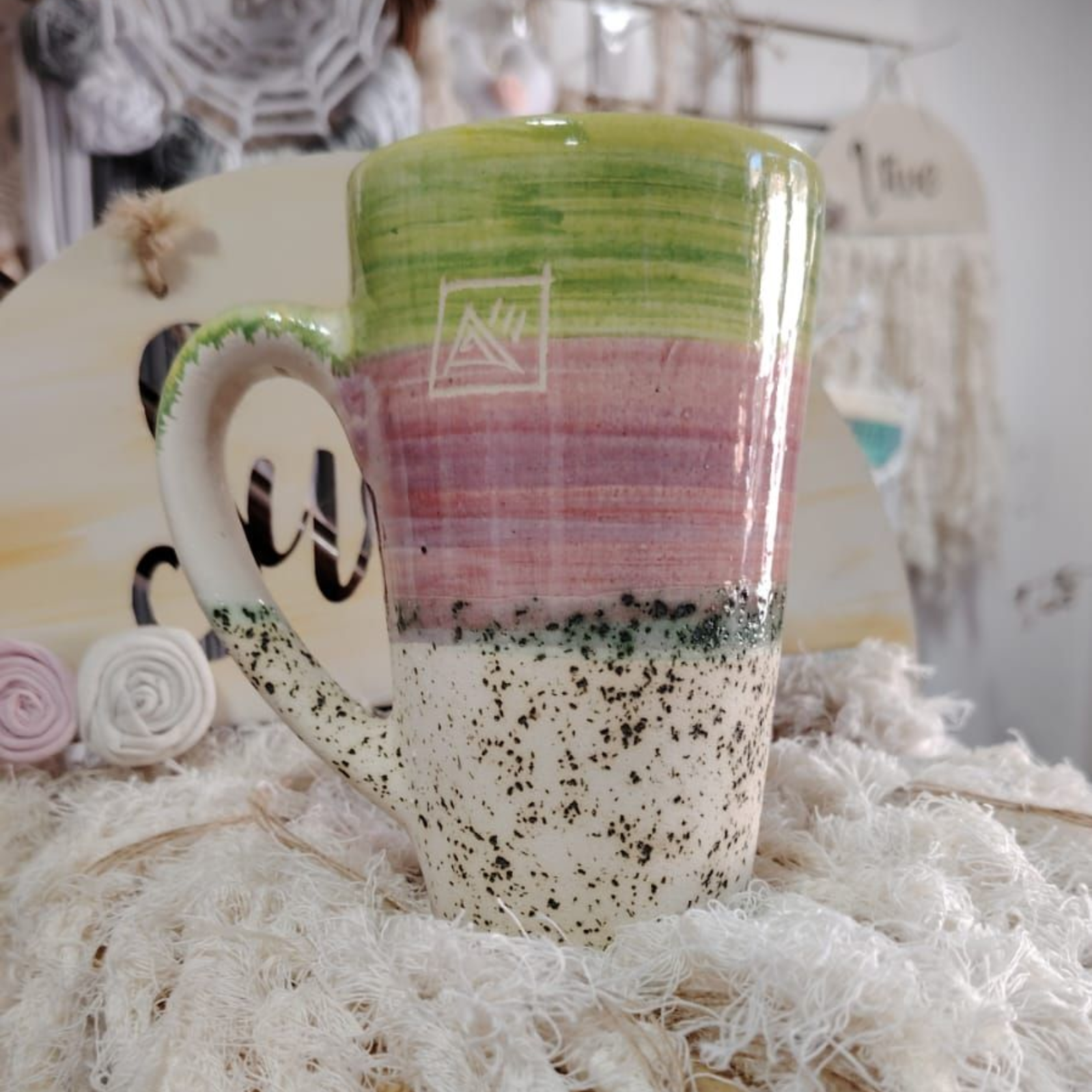 Taza de cerámica colorida con esmaltado verde, morado y blanco moteado, sobre una superficie tejida.