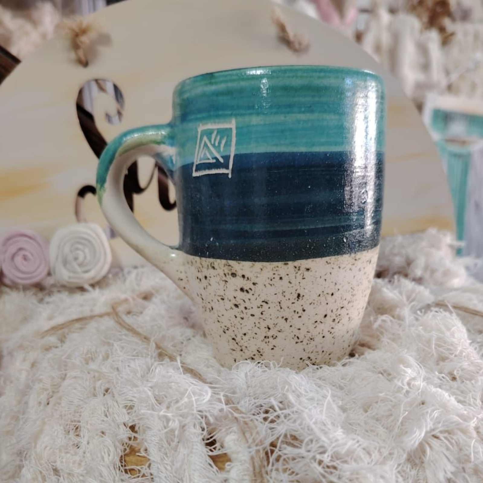 Taza de cerámica con esmaltado turquesa y azul marino sobre blanco moteado, colocada sobre un paño blanco.